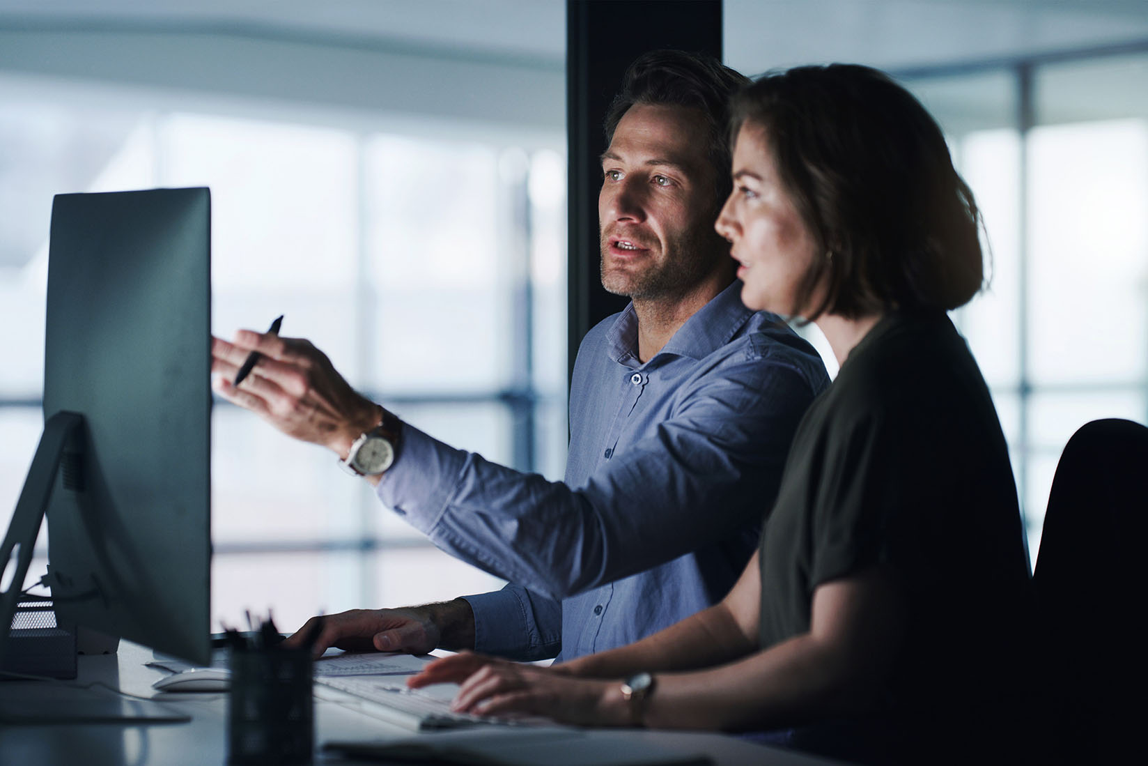 Shot of two businesspeople working together on a computer in an office at night