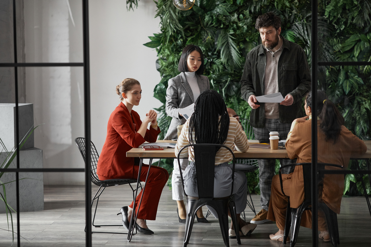 Graphic full length portrait of diverse group of business people meeting at table in modern office interior, copy space